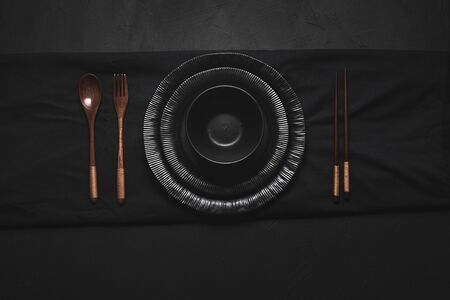 Empty plates and bowl and Asian bamboo cutlery on black tablecloth. Above view of black Japanese tableware with bamboo chopsticks on black background.の写真素材