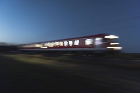 Red train in motion with light at windows, in the evening. Traveling by night. Train travel. Blur...