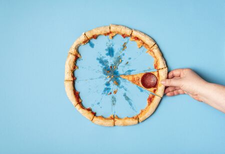 Woman taking a slice of pizza salami and pizza crust leftover, on blue background. Flat lay of eating pizza pepperoni. Last slice of pizza and crust.の写真素材
