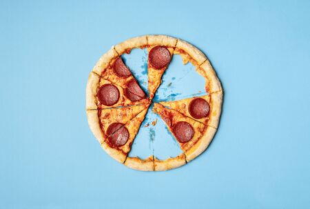Pizza pepperoni slices and leftover crust on blue background. Above view of sliced pizza salami with missing slices and crust leftover. Eating pizza.の写真素材