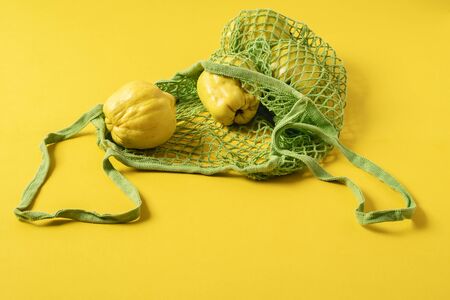 Fresh quince fruits in a net fabric bag on yellow background. Eco-friendly shopping bag and fruits. Reusable grocery bag. Reduce plastic pollution.の写真素材