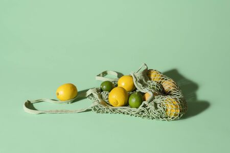 Lemons and limes in a reusable fabric shopping bag on green background. Eco-friendly net bag with...