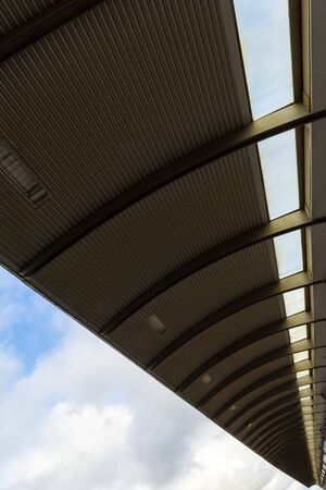 Bottom view of a metal roof from a train station platform. Steel roof construction under the blue...