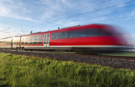 Modern red train, in motion blur, traveling through green nature, german countryside, on summer...