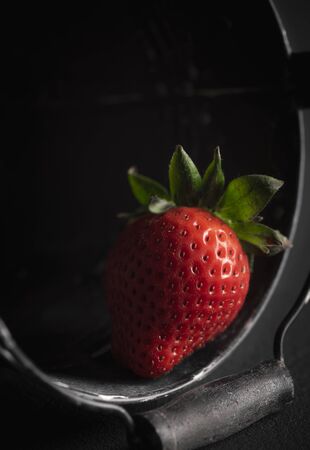 Organic strawberry close-up, collected in a black bucket, in low light. Red strawberry in a bucket. Summer fresh fruit. Healthy dessert. Sweet fruit.の写真素材
