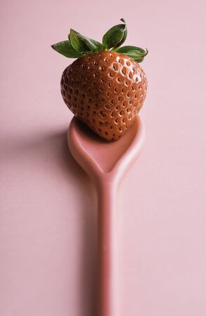 Ripe strawberry on a pink spoon, on a seamless background. One red berry close-up. Single organic strawberry. Sweet summer fruit.の写真素材