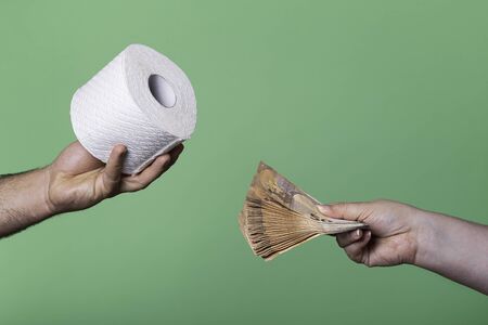 Woman offering a stack of money for a roll of toilet paper. Buying and selling concept with toilet paper and euro currency.の写真素材