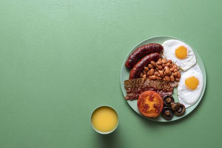 Traditional english breakfast with baked beans, sausages, bacon and sunny-side-up eggs on a green background. British full breakfast on a plate.の写真素材