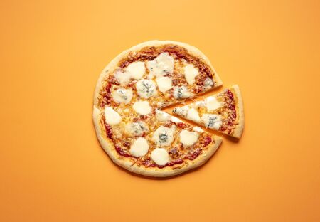 Pizza Quattro Formaggi homemade after an italian recipe. Classic plain pizza top view on an orange colored background. Pizza with a lot of mozzarellas, parmesan, and gorgonzola.の写真素材
