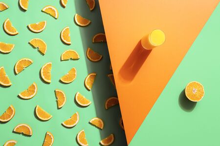 Summer drink, a glass of orange juice, and fruit slices on seamless green and orange background....