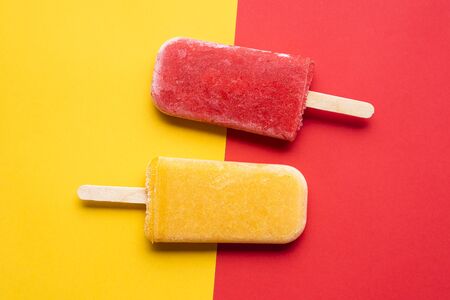 Two popsicles ice cream on a yellow and red background, above view. Flat lay with homemade icecream from fruitsの写真素材