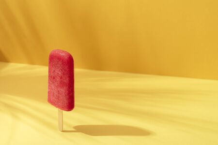 Strawberry ice cream  on a yellow background in sunlight. Cooling dessert. Red sorbet on a stick. Sunny tropical summer context.の写真素材
