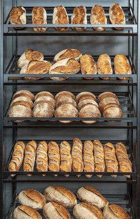 Freshly baked bread loaves on a metal rack inside a baker shop. Various types and sizes of white...