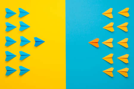Paper airplanes teamed up in 2 colors, blue and yellow, face to face in battle formation. A...