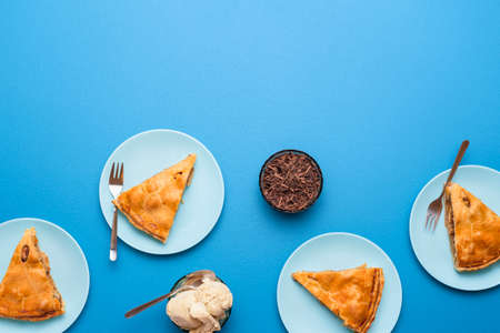 Apple pie slice with golden crust served with vanilla ice cream and a hot coffee on a blue table. Flat lay with an apple tart. Thanksgiving dessert.の写真素材