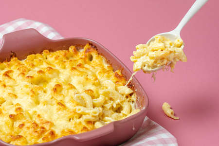 Grabbing a spoon of cheesy macaroni from the tray with macaroni and cheese freshly baked. Mac and...