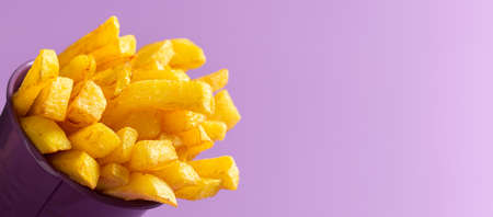 Close-up of french-fried potatoes in a bucket, isolated on a purple seamless background. Banner with...