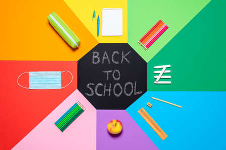 Above view with school props and face mask for a return to school during COVID-19 pandemic. School supplies on a multicolored background. Back to school in pandemic conceptの写真素材