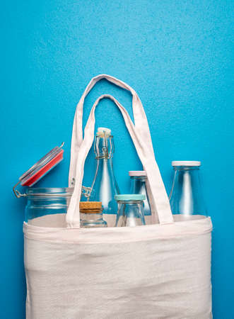 Top view with empty glass bottles and jars in a cotton shopping bag. Plastic-free bottles in a grocery bag on a blue background.の写真素材