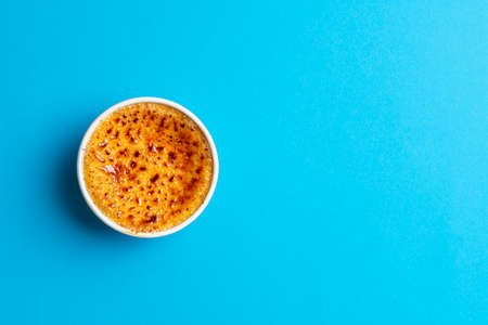 Single ramekins bowl with creme brulee on a blue background, above view. Delicious homemade dessert after a french recipe burned cream with caramelized sugar.の写真素材