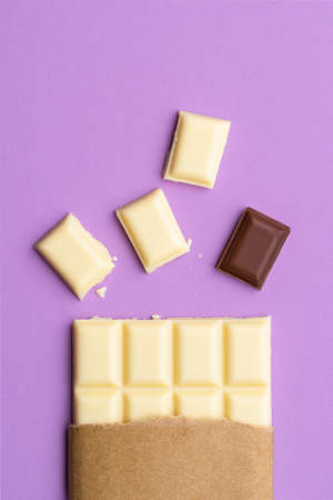 White chocolate pieces and milk chocolate isolated on a purple background. Stand apart from the...