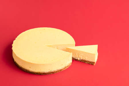 Homemade classic cheesecake with one slice, isolated on a red seamless background. Creamy dairy cake. Delicious Christmas dessert. Sliced cheesecake.の写真素材