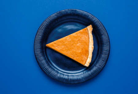 One slice of pumpkin pie on a plate, top view. Above view with a slice of pie on a blue background....