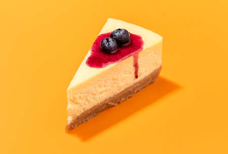 Cheesecake slice with blueberry syrup topping and creamy filling, isolated on an orange seamless background. Close-up of a single slice of cheesecake.の写真素材