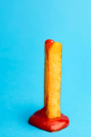 French fries with ketchup, one piece, isolated on blue seamless background. Close-up with a single potato french-fried in tomato sauce. Fast food.の写真素材