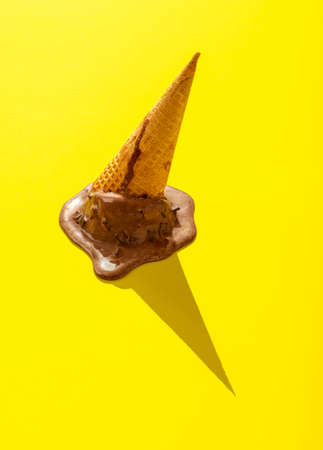 Upside down chocolate ice cream on a yellow background. Melting ice cream in bright light. Waffle cone ice cream isolated on a yellow-colored background.の写真素材
