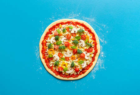 Above view with an uncooked pizza homemade with mozzarella, tomato sauce and fresh vegetables. Baking a pizza primavera flat lay.の写真素材