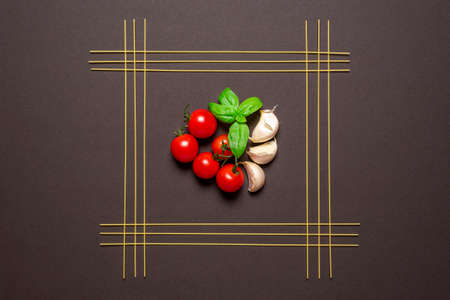 Uncooked spaghetti aligned symmetrically in a square and the tomato sauce ingredients in the middle, on a brown colored table. Raw spaghetti and fresh vegetables, tomatoes, garlic and basil for spaghetti sauceの写真素材