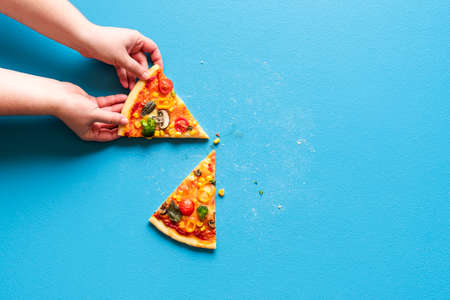 Woman's hand grabbing a slice of vegetarian pizza. Above view with slices of pizza primavera on a blue colored table.の写真素材