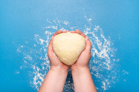 Leavened raw dough held in hand over a blue table. Flat lay with woman holding bread dough. Hand-kneaded donut batter. Baking sourdough bread.の写真素材
