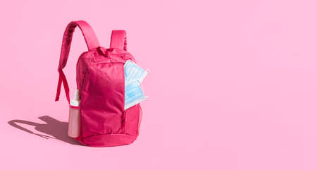 School reopening in the pandemic banner. Pink schoolbag with medical masks, isolated on pink...