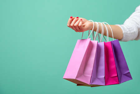 Colored paper bags on a woman's hands against a blue background. Young woman holding on her hand pink and purple shopping bags.の写真素材