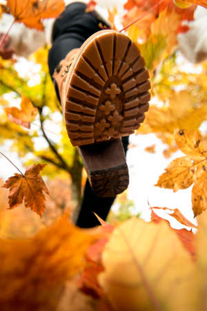 Close-up of a woman foot in boots, walking on autumn leaves. Playing with dry leaves. Autumn outdoor...