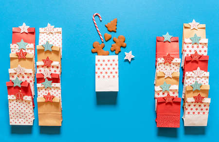 Making advent calendar gift bags with gingerbread cookies and candy canes, on a blue background. Top...