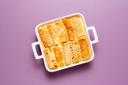 Top view with french pancakes rolls stuffed with curd cheese baked in a tray with sweet cream sauce. Delicious crepes roll filled with cheese.の写真素材