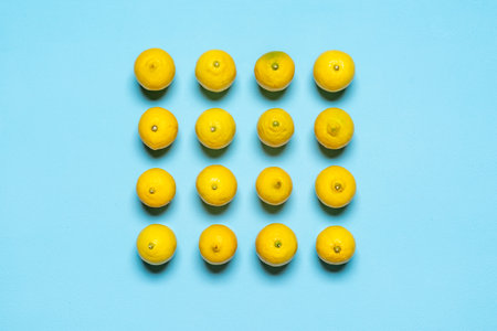 Above view with many lemons aligned symmetrically in a square on a blue background. Fresh lemons top...
