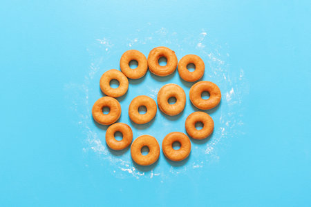 Yeast raised doughnuts aligned in a circle shape, on a blue background. Flat lay with ring donuts on the kitchen table. Homemade fried donuts.の写真素材