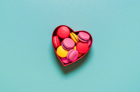 Above view with multi-colored homemade macarons in a red heart-shaped gift box, isolated on a green background.の写真素材