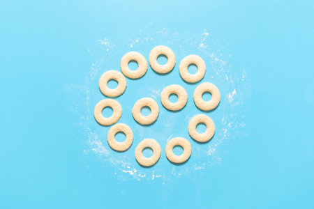 Raw donut dough cut in ring shapes, on blue background. Cooking doughnuts recipe. Homemade yeast raised donuts. Uncooked sweet dough. American sweets.の写真素材
