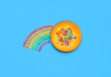 Bowl of multicolored cereals and a cereal rainbow, isolated on a blue-colored background. Breakfast...