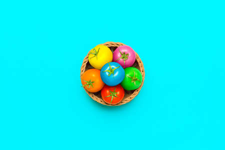 Colorful tomatoes in a basket, isolated on a blue-colored background. Flat lay with vegan Easter...