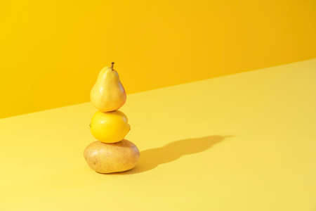 Minimal concept with potato, lemon, and a pear stacked on a yellow background in bright light. Yellow monotone image with vegetables and fruits.の写真素材