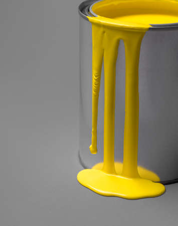 Close-up of a metal can and yellow paint dripping on it. Yellow paint drip and puddle on a gray background.の写真素材