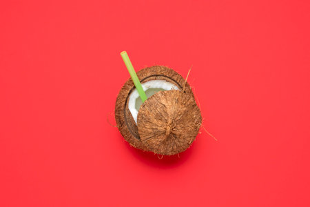 Top view with a cracked coconut isolated on a red background. Flat lay with a coconut with a drinking straw in it.の写真素材