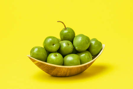 Close-up with a palm leaf bowl full of fresh green olives on a yellow table. Organic olives in a disposable bowl.の写真素材