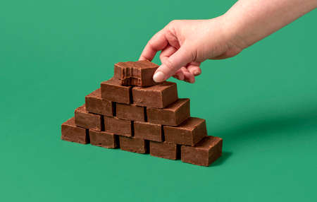 Minimalist shot with a woman's hand grabbing a chocolate fudge bar. Stack of fudge bars isolated on a green background.の写真素材